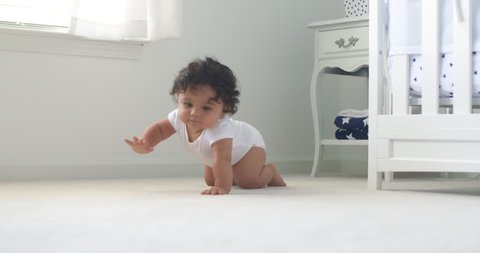 Baby Crawls Toward Rack Focus Low Angle Slow Motion. Baby crawls toward the camera in slow motion smiling and laughing in a white room
