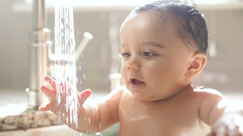 Baby in Awe of Water Stream from Sink Faucet. a stream of water pouring out of the faucet and baby looks at the water in amazement slow motion
