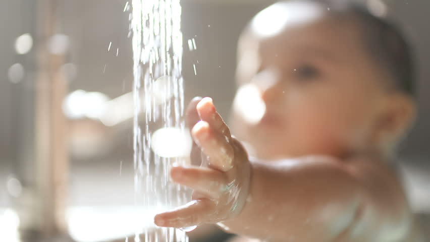 Baby Reaches for Faucet Water Rack Focus to Face. focus on baby's hand reaching under stream of water from the faucet then racks focus to the baby's face in awe of the water
