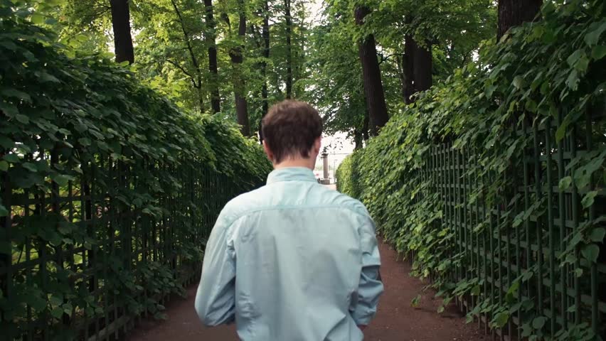Young man going at park using laptop receiving good news and celebrating success. Summer day. Freelancer working outdoors. Trees and green spaces at background.