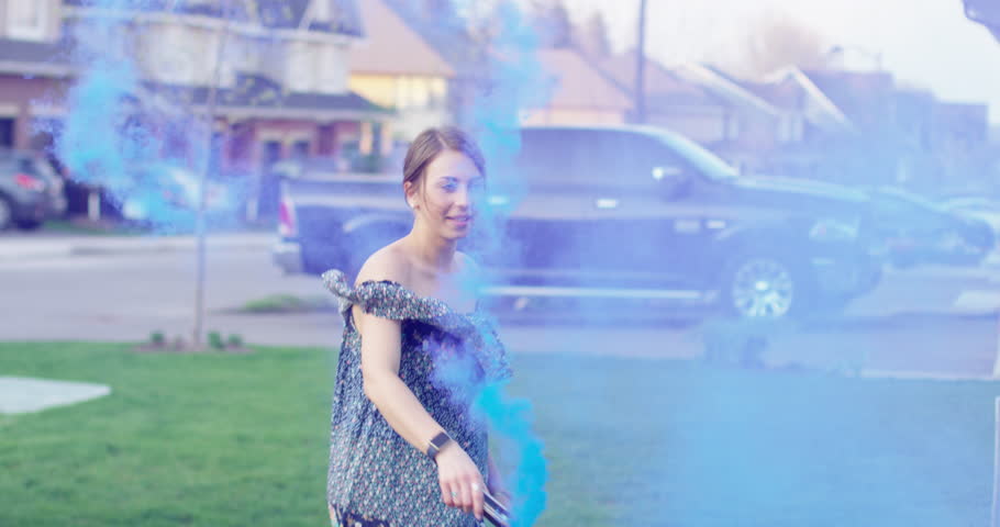 20s woman signs and dances in blue smoke in front yard celebration- slow motion