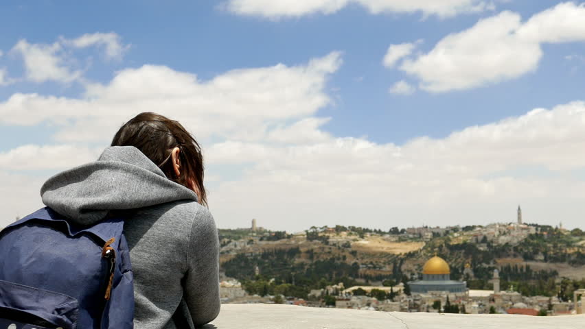 Longhair woman enjoys the Jerusalem cityscape outdoors in windy weather. Her hair is waving and flying in the wind.