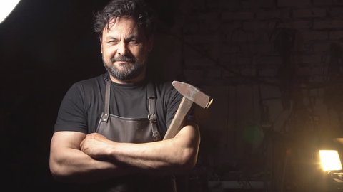Portrait of a man of a blacksmith in the working atmosphere. Brutal man looks and smiles at the camera. Slow motion