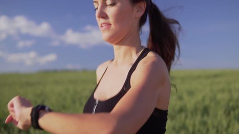 A young woman runner is runing across the field and looks at the heart rate monitor in slow motion