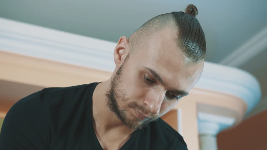Confectioner young brawny caucasian bearded man squeezes whiped creme puffs in line out sleeve onto cake layer on kitchen table