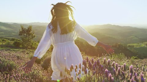 Beautiful woman wearing white dress running through beautiful purple lavender field at sunset. Golden hour.