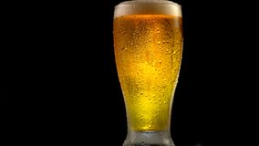 Cold Beer in a glass with water drops isolated on matte black background. Pint of light beer rotated. Craft Beer close up. Rotation 360 degrees. 4K UHD video 3840x2160