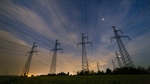Silhouette of four electricity pylons on the wheat field from beautiful sunset till nightly starry sky. Day to night time lapse of high-voltage power lines ends with flashes of lightning.