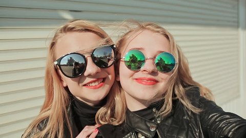 Two young beautiful girlfriends blonde in sun glasses on her face fun and coquettish posing in front of the camera. Do selfie. Spring.
