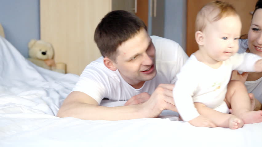 Happy family: father, mother and baby playful in the bedroom