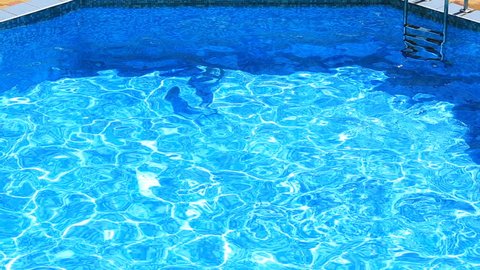 The child is swimming in the blue water of the pool. view from above. The girl dives into the water