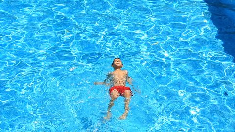 The child is swimming in the blue water of the pool. view from above.