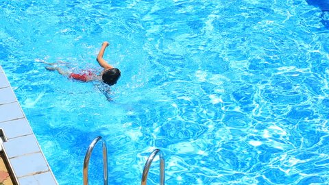 The child is swimming in the blue water of the pool. view from above.