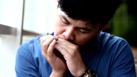 South east asian men playing music with harmonica in close up