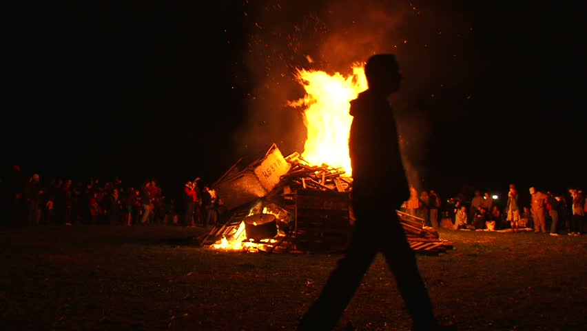 Many people watch as huge bonfire burns at night.