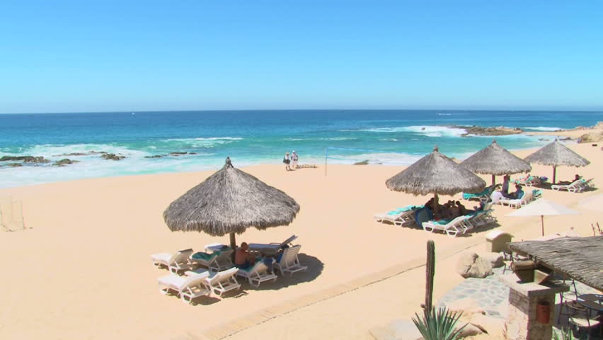 People enjoy perfect blue sky day at the beach by tiki huts in Cabo San Lucas,