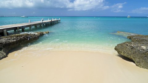 Caribbean beach background with turquoise water, pier, Grand Cayman island, and boats in the background.