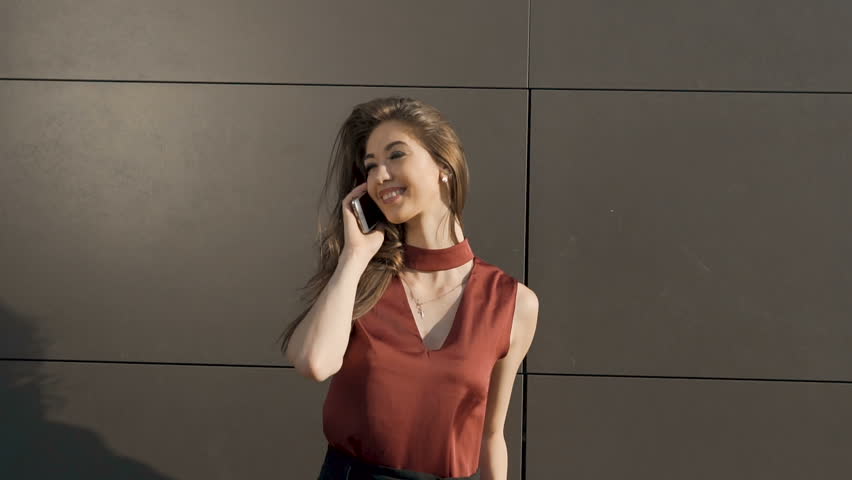 Sexy happy brunette with long hair kindly speaking by phone before dark wall, 120FPS slowmotion