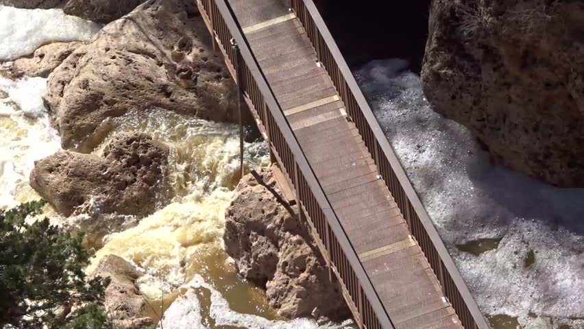 Turbulent water threatening a foot bridge in a flooded canyon; includes the natural ambient sound of the water (volume reduced); Pine Creek in Tonto Natural Bridge State Park in Arizona