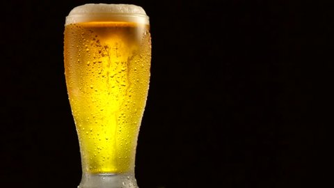 Cold Light Beer in a glass with water drops over matte black background, border design. Craft Beer close up. Pint of beer. Copy space for your text. Rotation 360 degrees. 4K UHD video 3840x2160