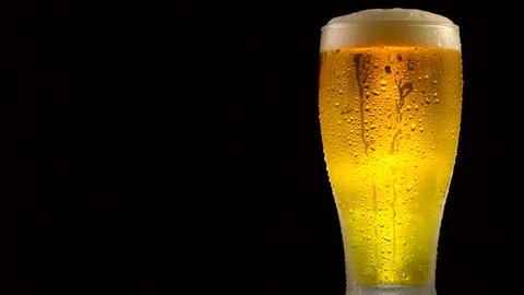 Cold Light Beer in a glass with water drops over matte black background, border design. Craft Beer close up. Copy space for your text. Rotation 360 degrees. 4K UHD video 3840x2160