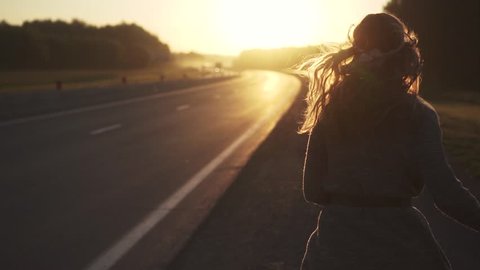 girl in the hippie clothes runs on the road at dawn. girl is on the road at dawn. young attractive woman in hippie clothes smiling and looking at camera. slow motion