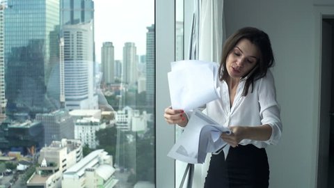 Angry businesswoman throwing documents while talking on cellphone in office, super slow motion 240fps
