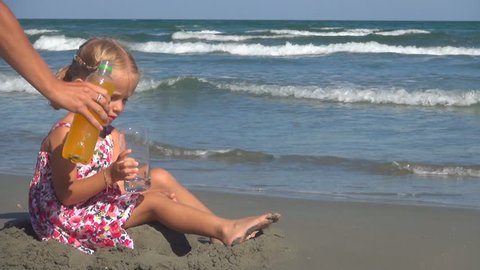 Mother Pouring Orange Juice to her Little Girl, Child Drinking Juice on Beach