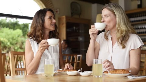 Two beautiful mature women holding cup of coffee and talking to each other in a cafeteria. Senior women in conversation while having breakfast. Happy middle aged friends meeting up for coffee. 