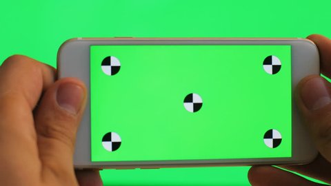 Male hand holding white cell phone with green screen on green background. Tracking motion. Chroma Key. Horizontal. Very close up