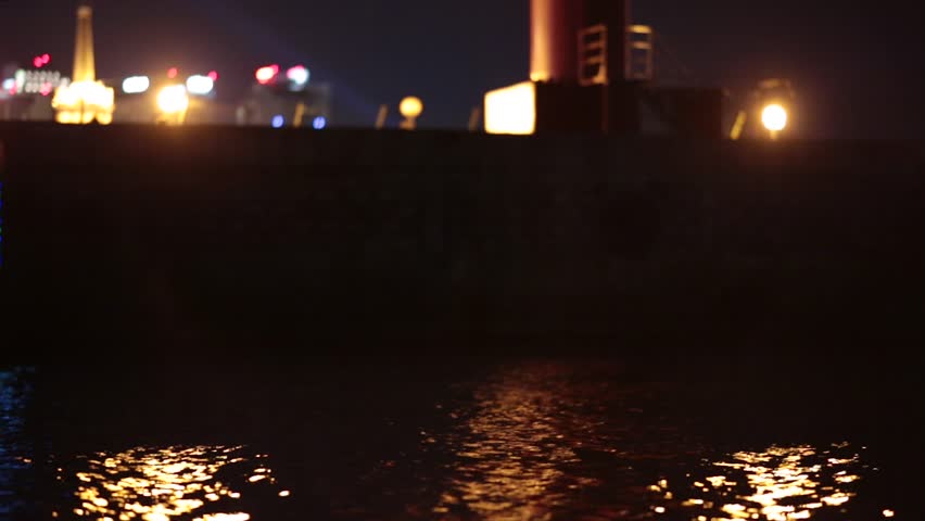 Illuminated river bus floating on waves at night.