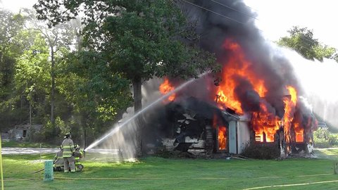 Firemen direct a high power water hose on a full blown fire during a control burn of an old house.