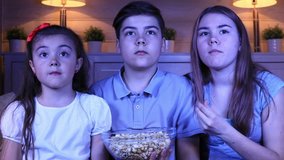Group of children watching a horror film on TV in the evening indoors
