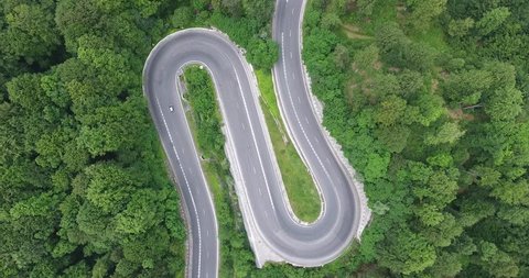 Hairpin turn in the forest. Aerial view of a curved winding road with cars passing
