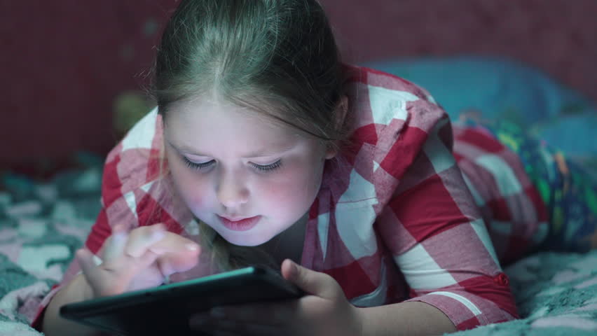 Caucasian girl playing game on tablet and lying on the sofa in the evening. | Shutterstock HD Video #28432036