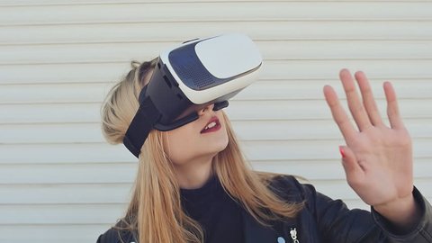 Young and stylish blonde in virtual glasses at a white wall.