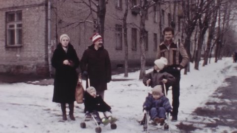 SAINT PETERSBURG, RUSSIA, 1985: Old vintage color film two families with kids on baby carriage walking in dormitory area on winter snowy day