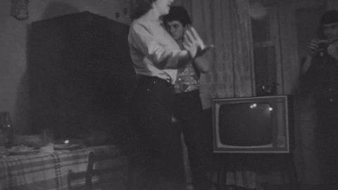 SAINT PETERSBURG, RUSSIA, 1981: Old vintage black and white film friends have party dancing in apartment living room, smoking cigarette