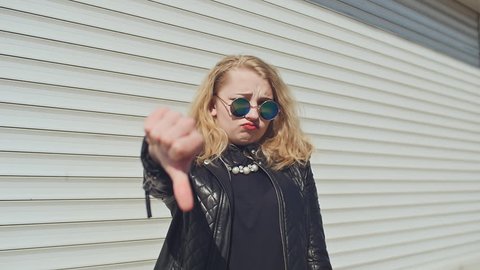 Stylish young girl on a white background shows a thumbs-down, do not like. Background of white horizontal rolling shutters.