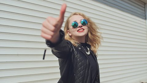 Happy young girl showing thumbs up. Hand gesture is super. Background of white horizontal rolling shutters.