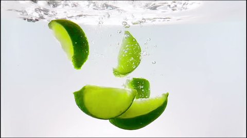 lime slice fruit splash falling down into white cocktail and water drinking glass, shot in slow motion on white background, fun, nutrition and drink concept