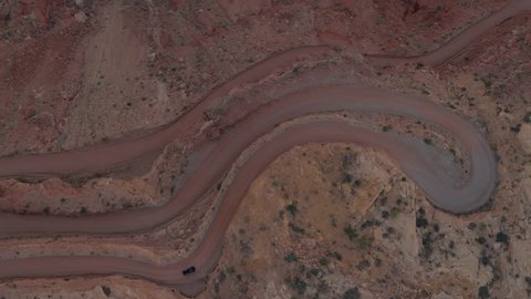 AERIAL TOP DOWN: Black SUV car driving up a winding switchback road on mesa mountain cliff in red rock desert. 4x4 jeep vehicle traveling on dangerous hairpin Moki Dugway carved into the cliff edge
