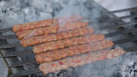 Several raw traditional Turkish shish Adana Kebab skewers that made of meat are lined up over charcoal in barbecue.