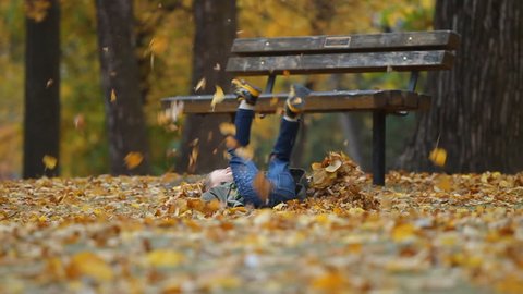 Стоковое видео: Running seven year old boy throws autumn leaves and falls to the ground. slow motion. 