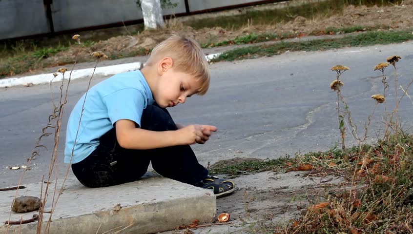 little boy gathers pebbles, twigs and leaves and throws them under the concrete slab