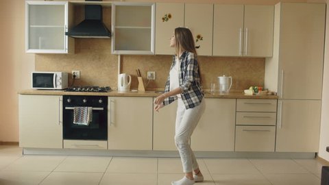 Cheerful young funny woman dancing and singing with ladle while having leisure time in the kitchen at home