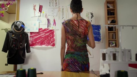 Hispanic woman at work as fashion designer and tailor, looking at sketches in atelier. Sequence