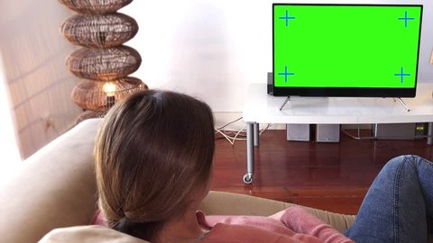 Girl On Phone Watching TV, Panning Shot. Young woman talks on the phone while watching television green screen. Shot behind models shoulders