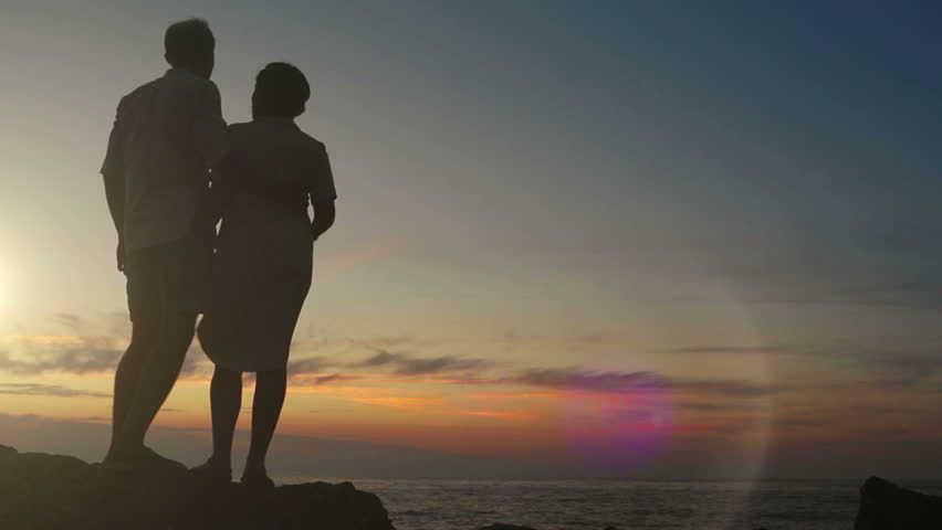Couple stands on the rock at sunset holding hands