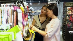 The lovely girl talks at the office about business relations to the visitor. Two girls choose color of fabric from samples at the stand.